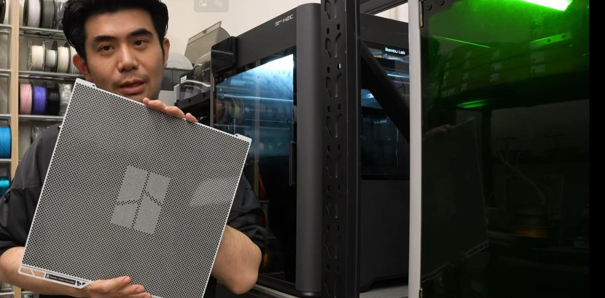 Big Bro holding a Bambu Vision Encoder calibration plate in front of a Bambu printer