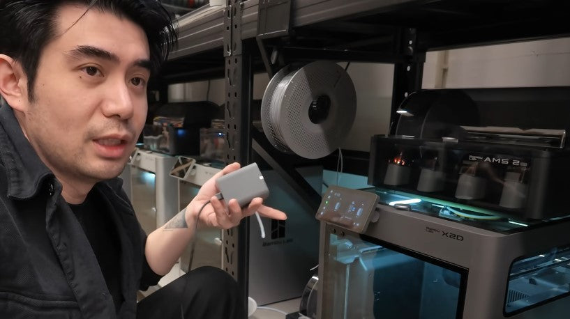 Big Bro holding a TPU Feeding Module in front of a Bambu Lab X2D printer.