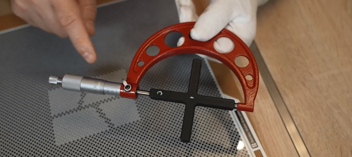 Measuring a small cross-shaped calibration print with calipers to check X/Y dimensional accuracy.